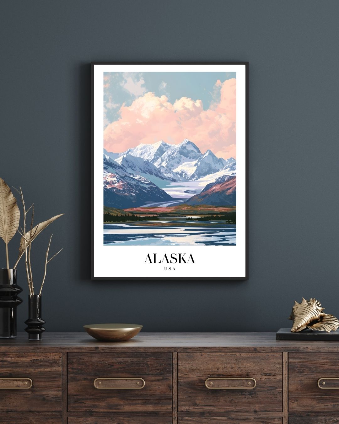 Framed poster of a mountain landscape with 'Alaska' text on a dark wall above a wooden cabinet.
