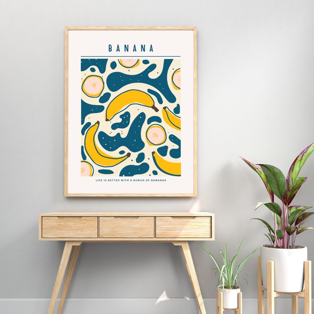 Framed banana-themed artwork on a wall above a wooden console table with plants.